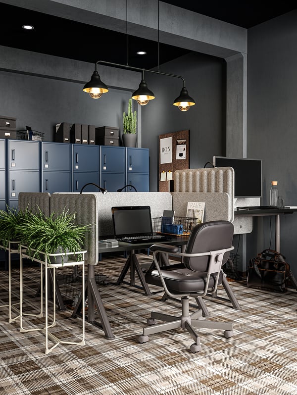 Modern office space with desks, chairs, screens, plants, and lockers, illuminated by pendant lamps.