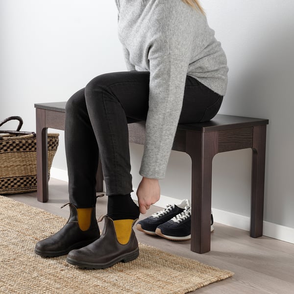 Person sitting on wooden bench, changing from black boots to sneakers.
