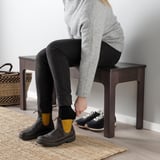 Person sitting on wooden bench, changing from black boots to sneakers.