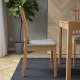 A dining chair with a slatted wooden back and cushion seat, positioned near a table.