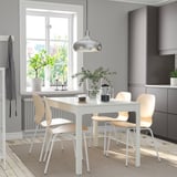 Modern dining room with extendable table, chairs, kitchen units, and decor near a large window.