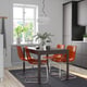 Modern kitchen with dark table and orange chairs, white pendant light, and potted plant on the windowsill.