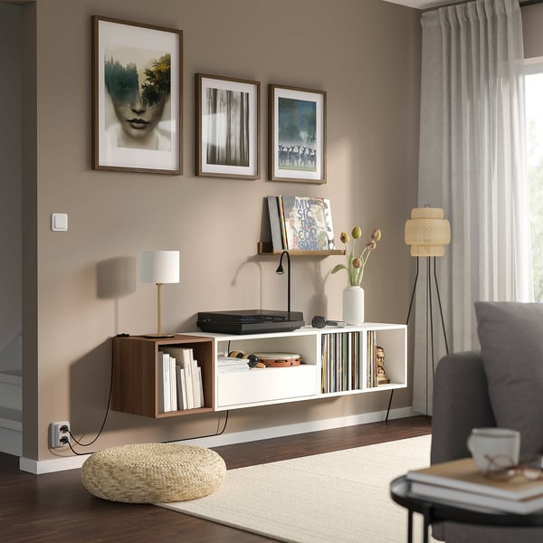 Modern living room with EKET shelf, record player, books, lamp, and art. Grey couch, standing lamp, and sheers by window.