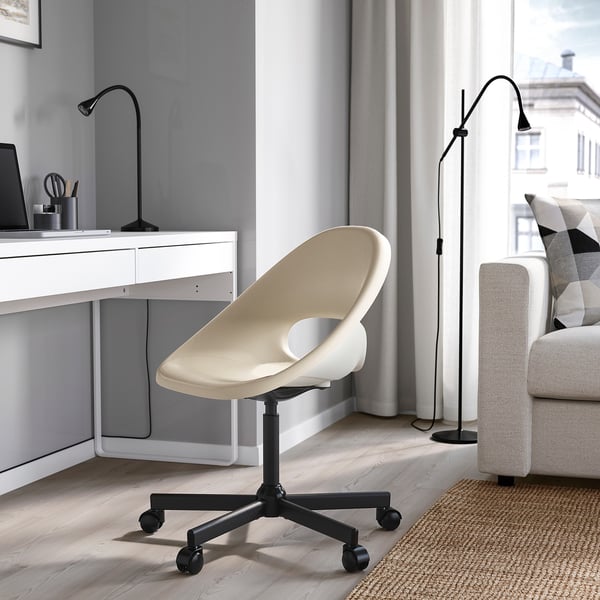 Modern home office with ELDBERGET chair, beige. Unique curved design, adjustable height, sturdy wheels. Positioned near desk with lamp, gray walls.
