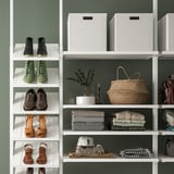 Organized closet with shoes, clothes, wicker bag, and decorative items on white shelves.