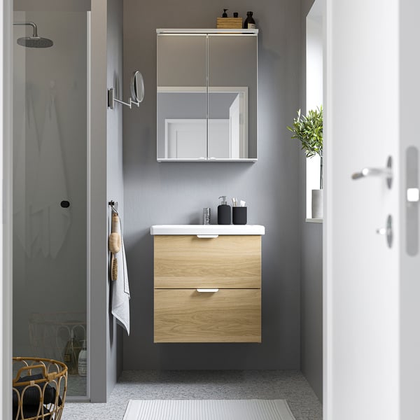 Modern, light wood bathroom vanity with mirror cabinet. White counter, black accents. Sleek, compact design.