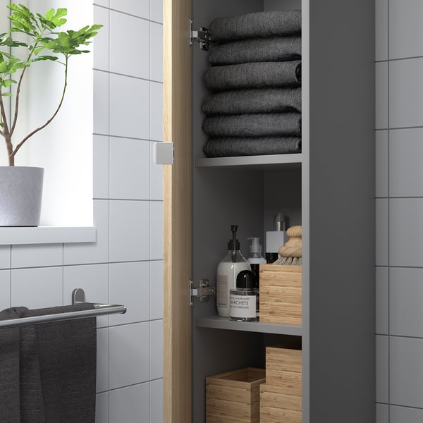 Modern bathroom cabinet with stacked dark towels, toiletries, and wooden boxes, offering ample storage.