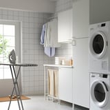 Modern laundry setup with white ENHET cabinets, stacked washer/dryer, clothes, ironing board, and storage.
