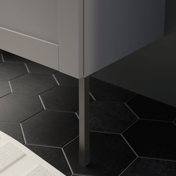 Modern gray bathroom cabinet on metallic legs, placed on black hexagon tiles.