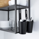 Black shelf organizer with containers for kitchen utensils and shelves with plates and glasses.
