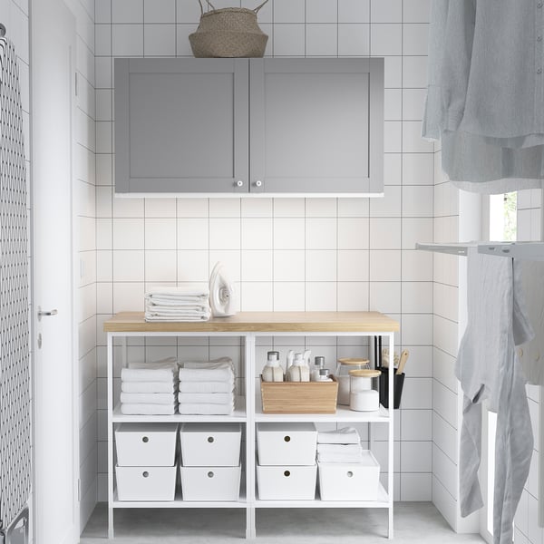 Compact laundry room with white tiles, gray cabinet, and organized shelf with towels, cleaning supplies, and an iron.
