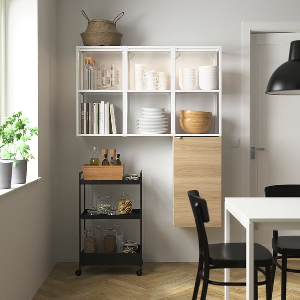Modern kitchen: white ENHET shelves & black cart, displaying dishes, jars, & books. Black chair & hanging lamp nearby.