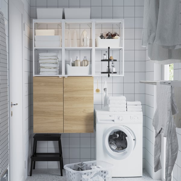 Modern laundry area with ENHET cabinet: sleek white, wood doors, height matches washing machine, shelves hold towels & bottles.