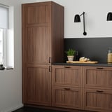 Modern kitchen with tall brown walnut ENKÖPING cabinets, sleek black countertop, and minimalist decor.
