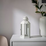 ENRUM white lantern with cutouts on console table, next to vase and chair.