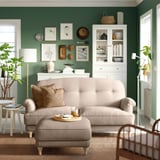 Modern living room: beige ESSEBODA sofa, green walls, white cabinet, wooden chair, floor lamp, plants, coffee table with tray.
