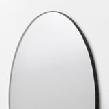 Oval mirror with sleek border, wall-mounted, reflecting light softly.