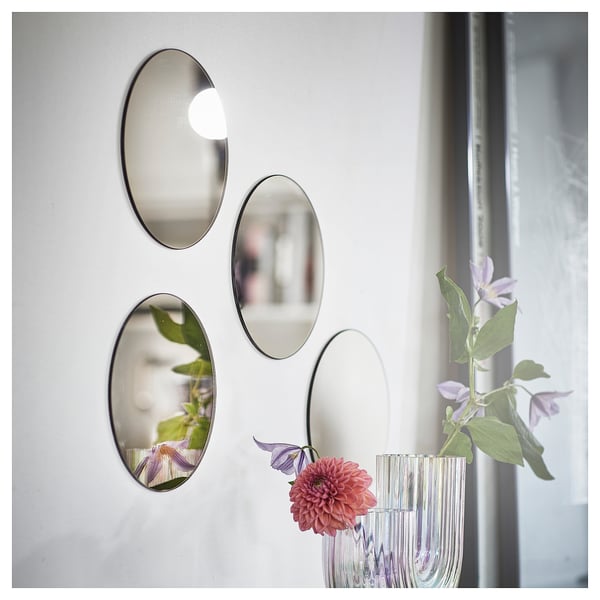 Four oval mirrors on white wall reflecting flower vase with pink-purple flowers.