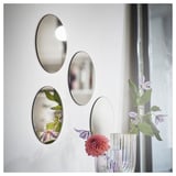 Four oval mirrors on white wall reflecting flower vase with pink-purple flowers.