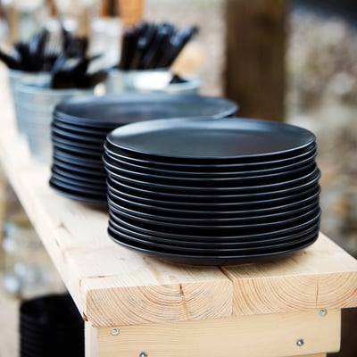 Black plates stacked on table with cutlery.