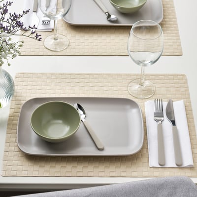 Table set with FÄRGKLAR plates, bowls, cutlery, and wine glasses on woven placemats.