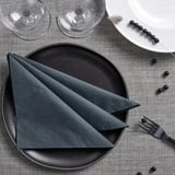 Black napkins, plate, glasses, fork, beads on grey linen.