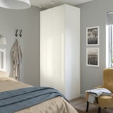 Modern bedroom with white glossy FARDAL wardrobe, beige bed, and a yellow chair. Two framed photos hang on the wall.