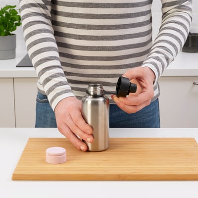 Person placing a black lid on a silver sports bottle on a cutting board.