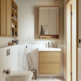 Modern bathroom with FAXÄLVEN mirror cabinet, sink, toilet, and cream tiling. Large mirror with lighting, hanging towel, and storage.