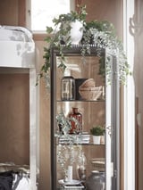 Display shelf with potted plants, books, vases, and baskets. White and green color scheme. Decorative, wooden backdrop.