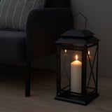 Candle in lantern beside couch, warm ambiance.