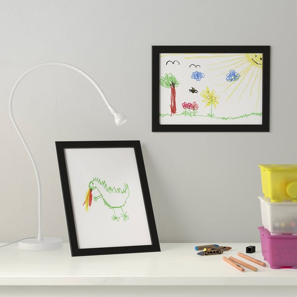 Frame with kids dinosaur drawing on table, art supplies; above, sun scene on wall.