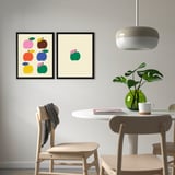 Colorful fruit prints above dining table with chairs, plant, and cup.