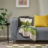 Gray sofa with striped green and white blanket, yellow pillow, and plant.