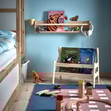 Childrens room with light blue walls; FLISAT wooden book rack, light wood; toys and books displayed; play mat with wooden blocks and train track.