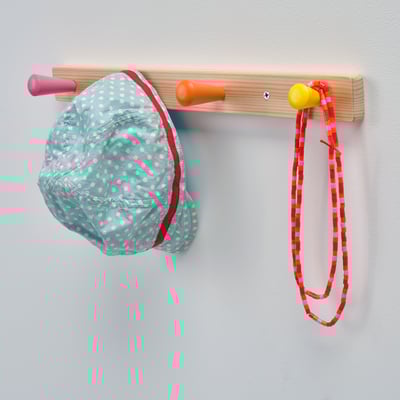 Wooden rack with 3 colorful knobs holding a polka dot face mask and a striped ribbon.