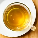 Clear glass mug filled with steaming green tea on a white saucer.