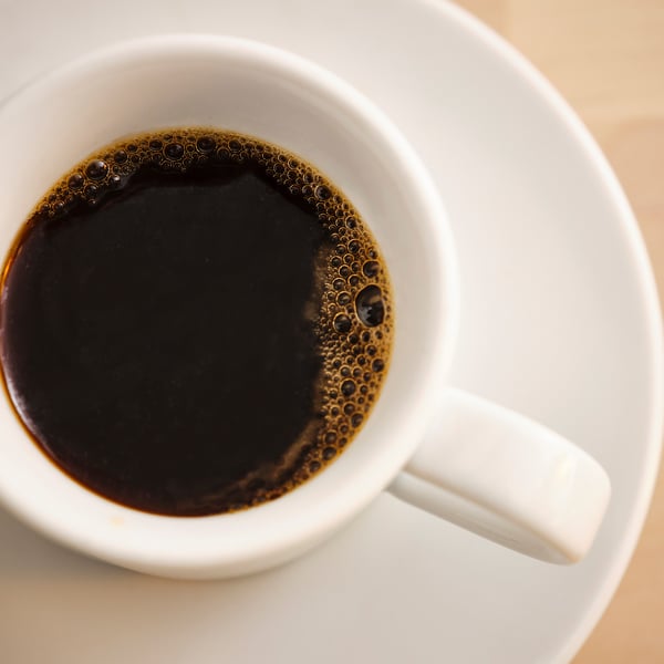 Close-up of cup filled with dark, bubbly liquid. The white ceramic mug has a handle, suggesting a hot beverage.