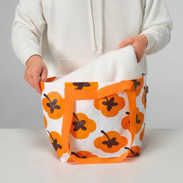 Person holding FÖSSTA reusable shopping bag, orange floral pattern, with white cloth inside.
