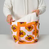 Person holding FÖSSTA reusable shopping bag, orange floral pattern, with white cloth inside.