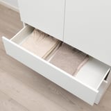 White cabinet drawer slightly open, revealing neatly folded clothes inside. Part of a platsa system for organized storage.