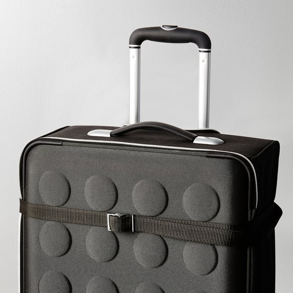 Black suitcase with raised circles, pull handle up, ready to travel. Strap and buckle visible, securing contents.