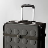 Black suitcase with raised circles, pull handle up, ready to travel. Strap and buckle visible, securing contents.