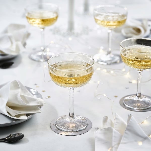 Table set with wine glasses, white napkins, and stainless steel coasters. Coasters feature a decorative, festive design.