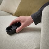 Persons hand holding a black reusable lint brush against a light-colored fabric.