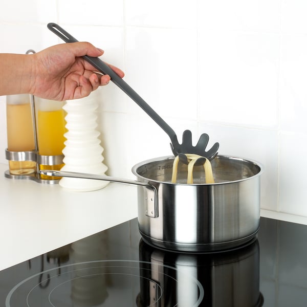 A hand uses a FULLÄNDAD silicone spatula, gentle on non-stick pots, to stir a yellow sauce on a stove.