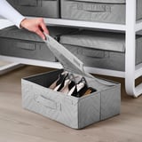 A person pulling out a grey FULLSMOCKAD shoe box from a white shelf, showcasing the boxs handles for easy lift.