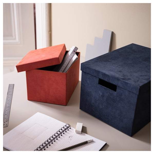Two red & blue GJÄTTA boxes on desk. One open showing rulers. Notebook with pen & eraser in front.