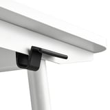 Close-up of modern desks underside. Black u-shaped clip holds tabletop; smooth white surface and clean lines shown.