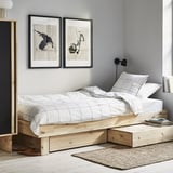 Modern bedroom with light wooden platform bed, white grid-patterned bedding, abstract wall art, and a rug.